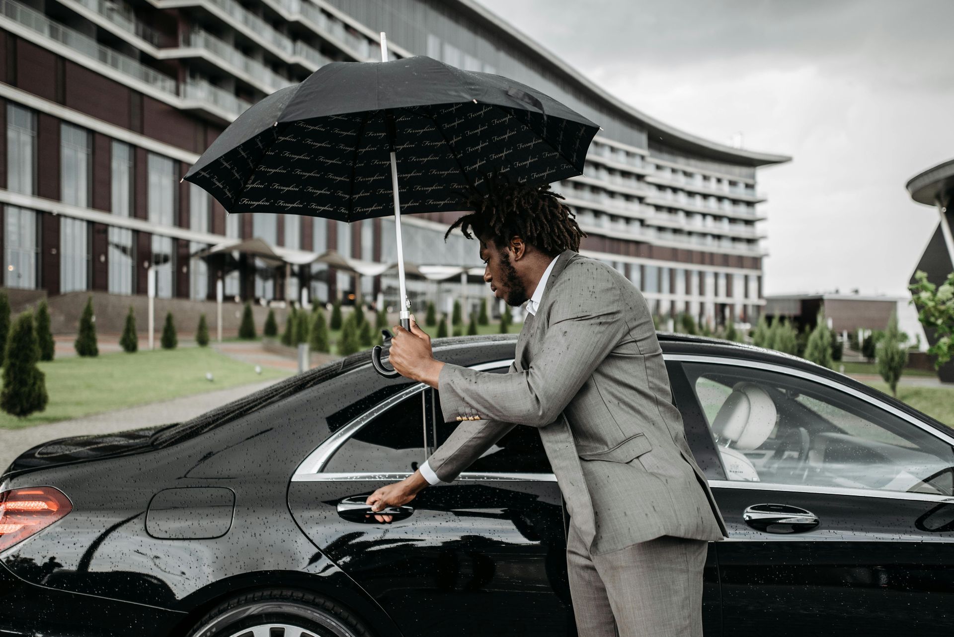 Man in suit opening car door under umbrella in front of a building.