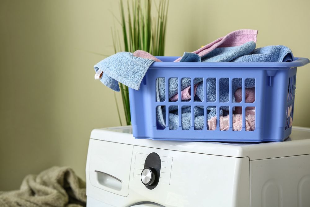 Una cesta de ropa sucia llena de toallas azules y rosas reposa sobre una lavadora.