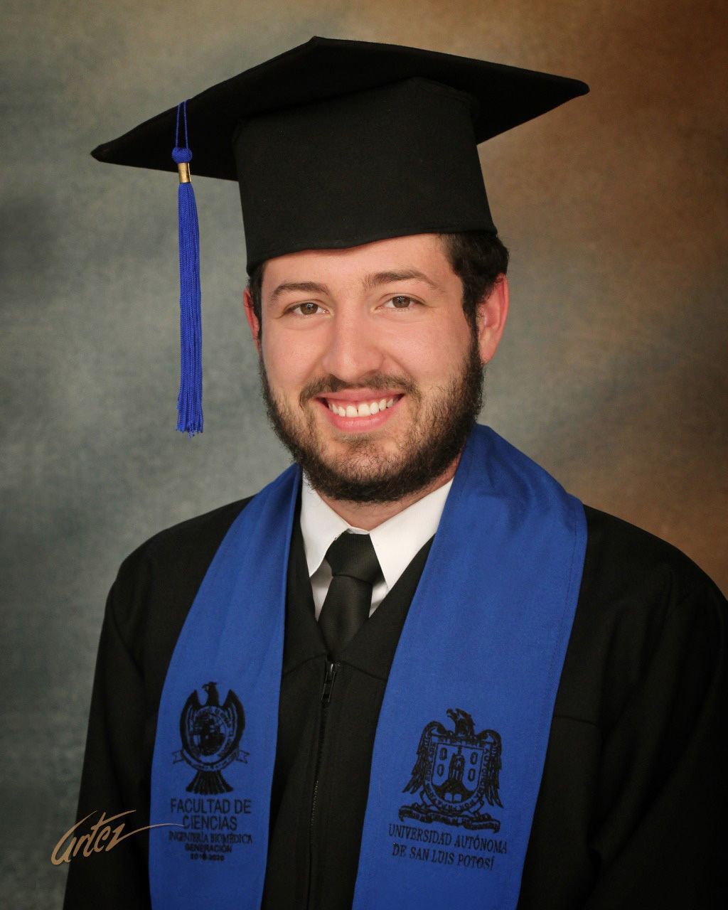 Un hombre vestido con toga y birrete de graduación está sonriendo
