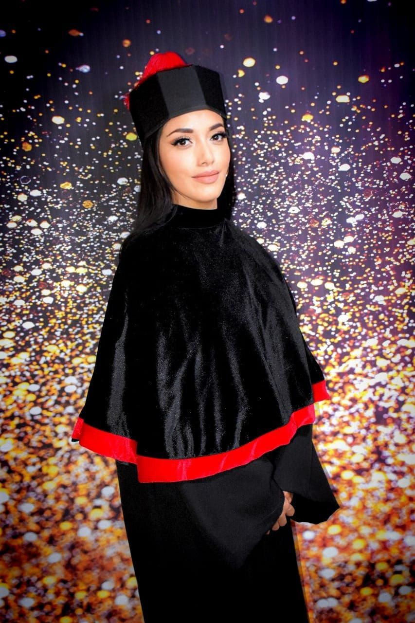 Una mujer con toga y birrete de graduación posa para una fotografía.