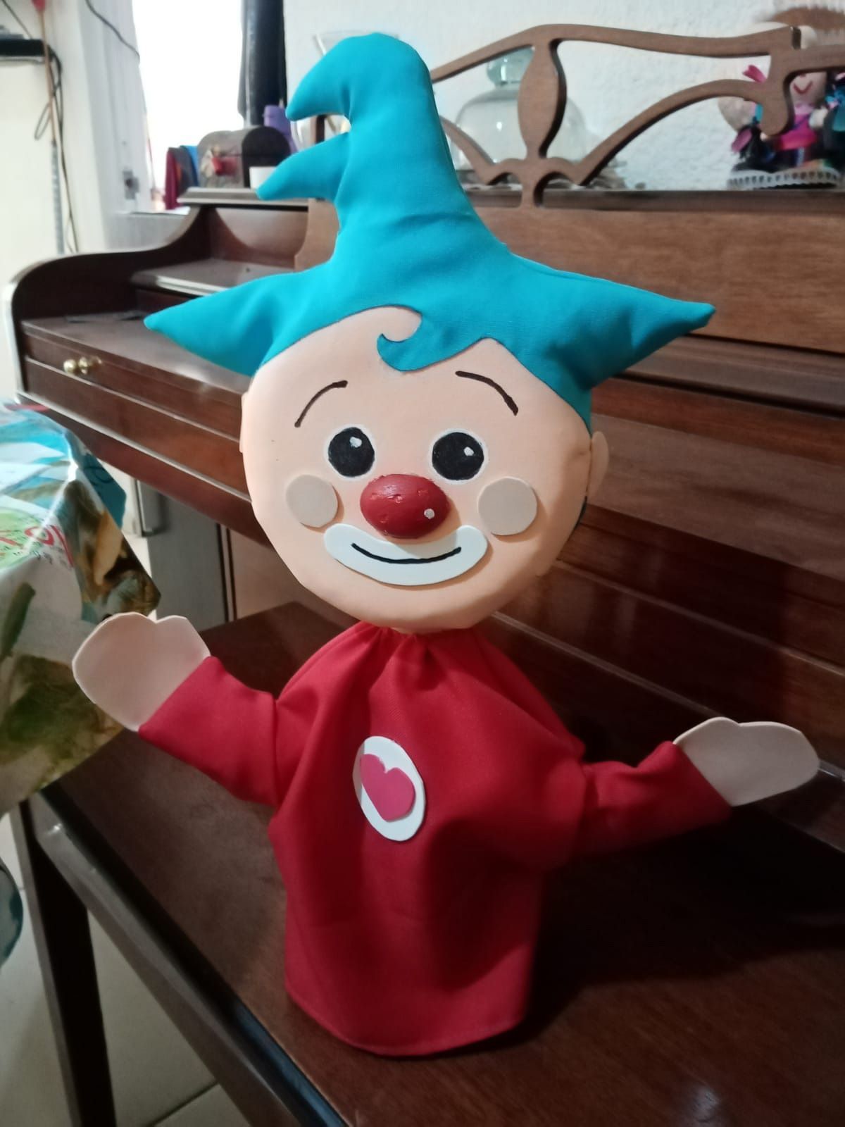 Un payaso con pelo azul y una camisa roja está sentado sobre una mesa de madera