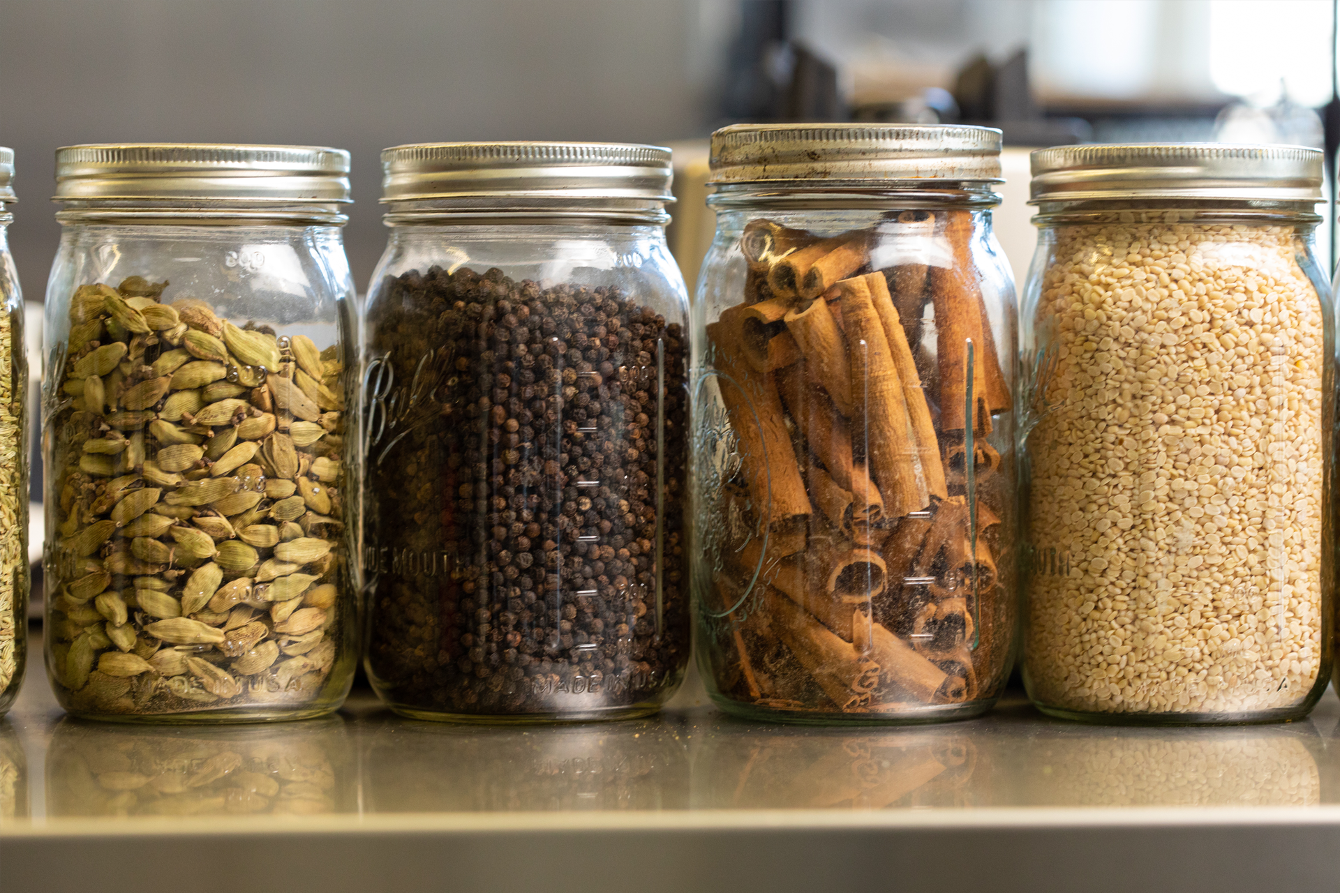 A row of jars filled with different types of spices on a shelf.