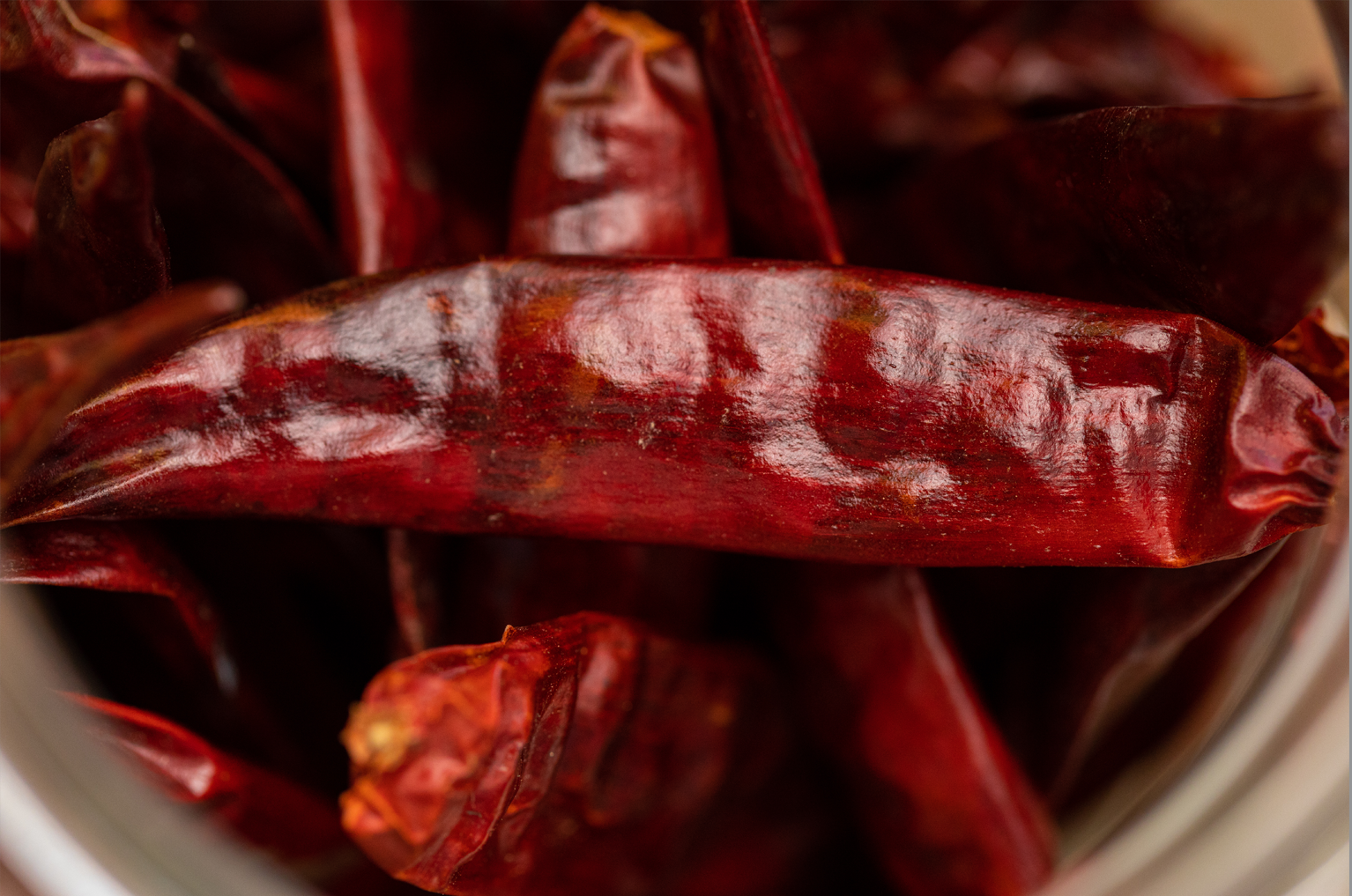 A close up of dried red chili peppers in a glass jar.