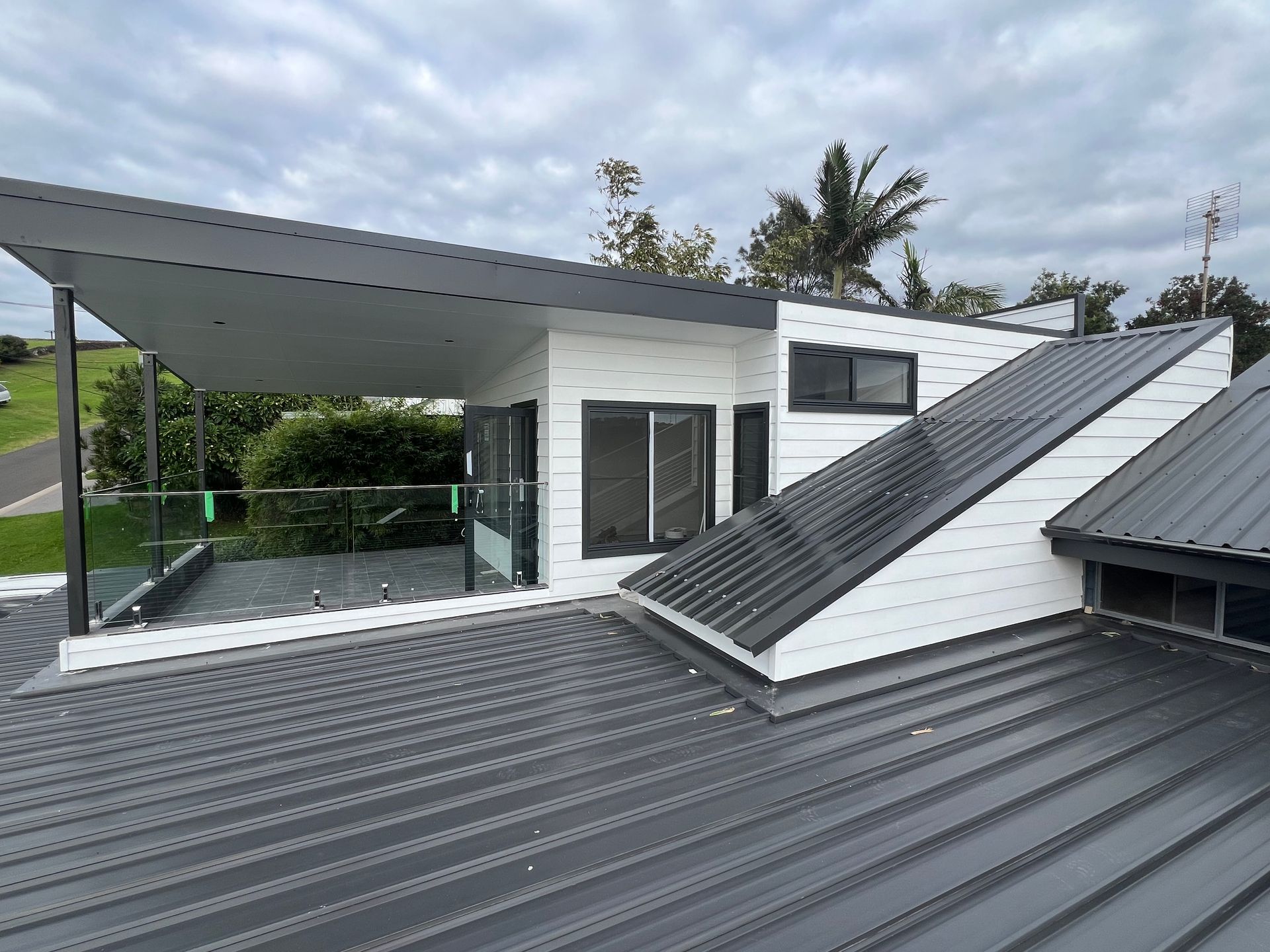 Modern white house with gray metal roof and rooftop terrace, surrounded by greenery.  — Taddeo Constructions in Kiama Downs, NSW