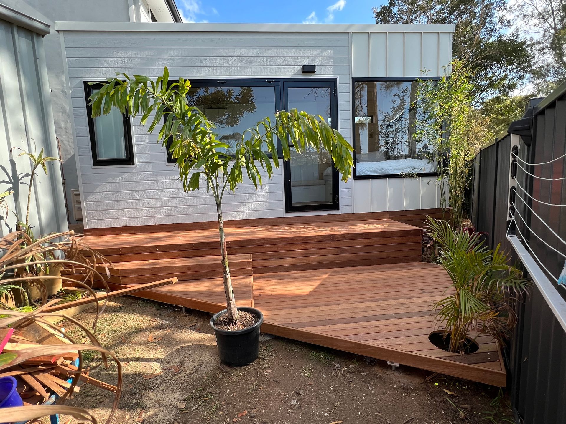 Backyard deck with brick steps, a small potted tree, and a modern white house exterior  — Taddeo Constructions in Kiama Downs, NSW