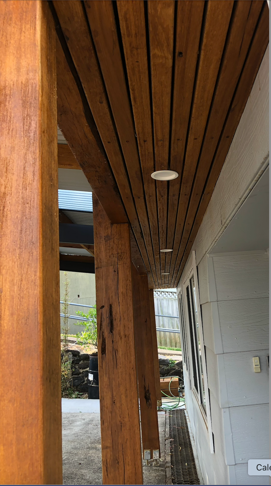 Wood-paneled porch ceiling with recessed light, supported by a wooden post beside a white wall. — Taddeo Constructions in Kiama Downs, NSW
