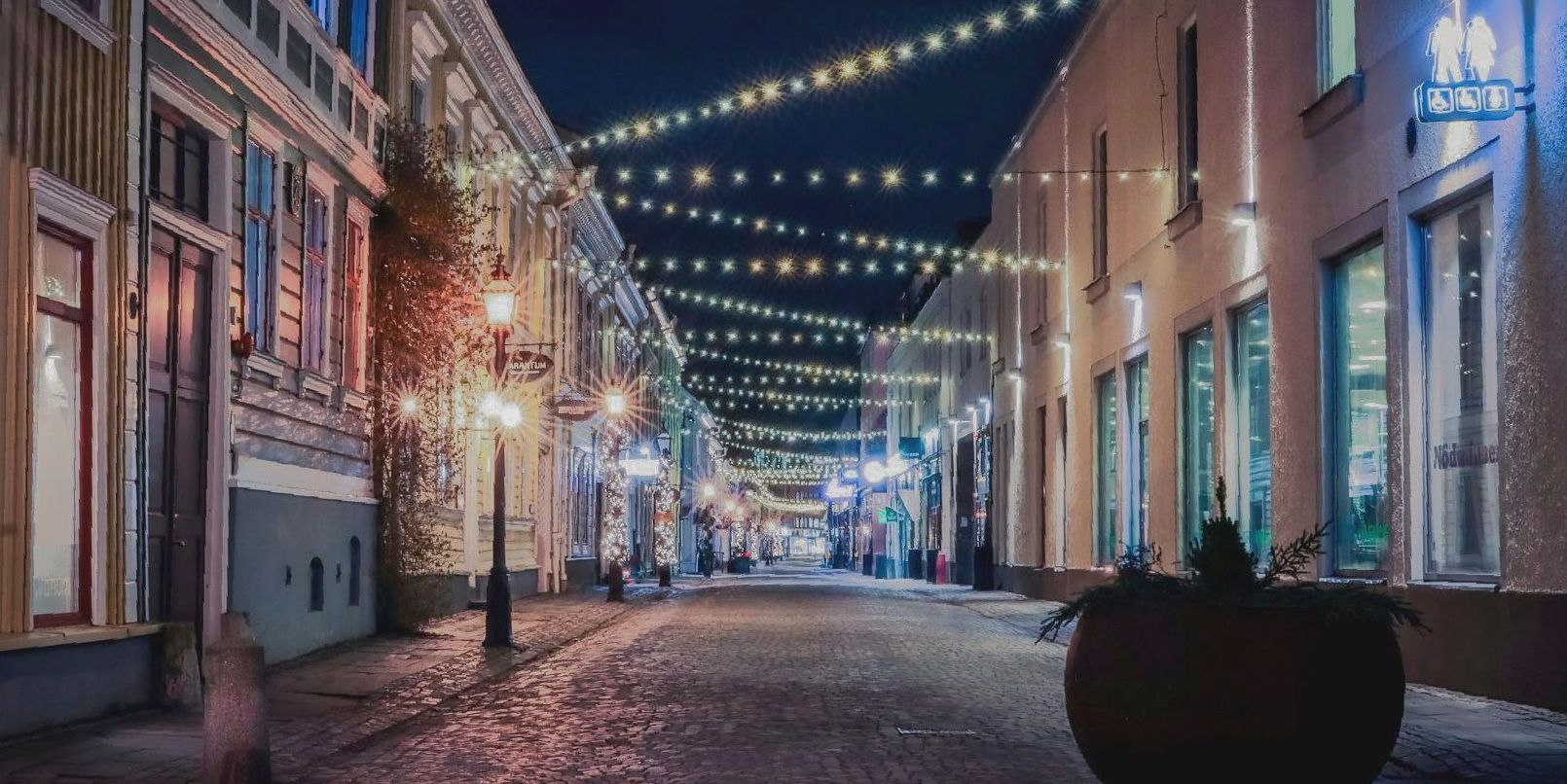A narrow street with lots of lights on the buildings at night.