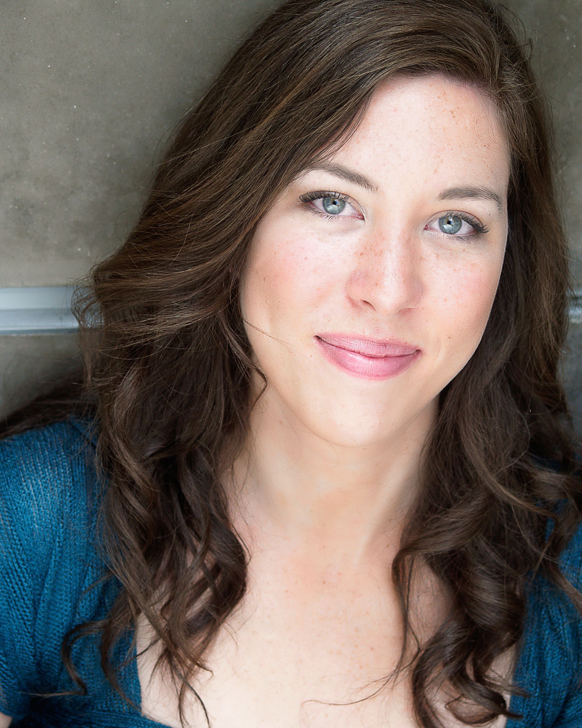 A woman with long brown hair is wearing a blue shirt and smiling for the camera.
