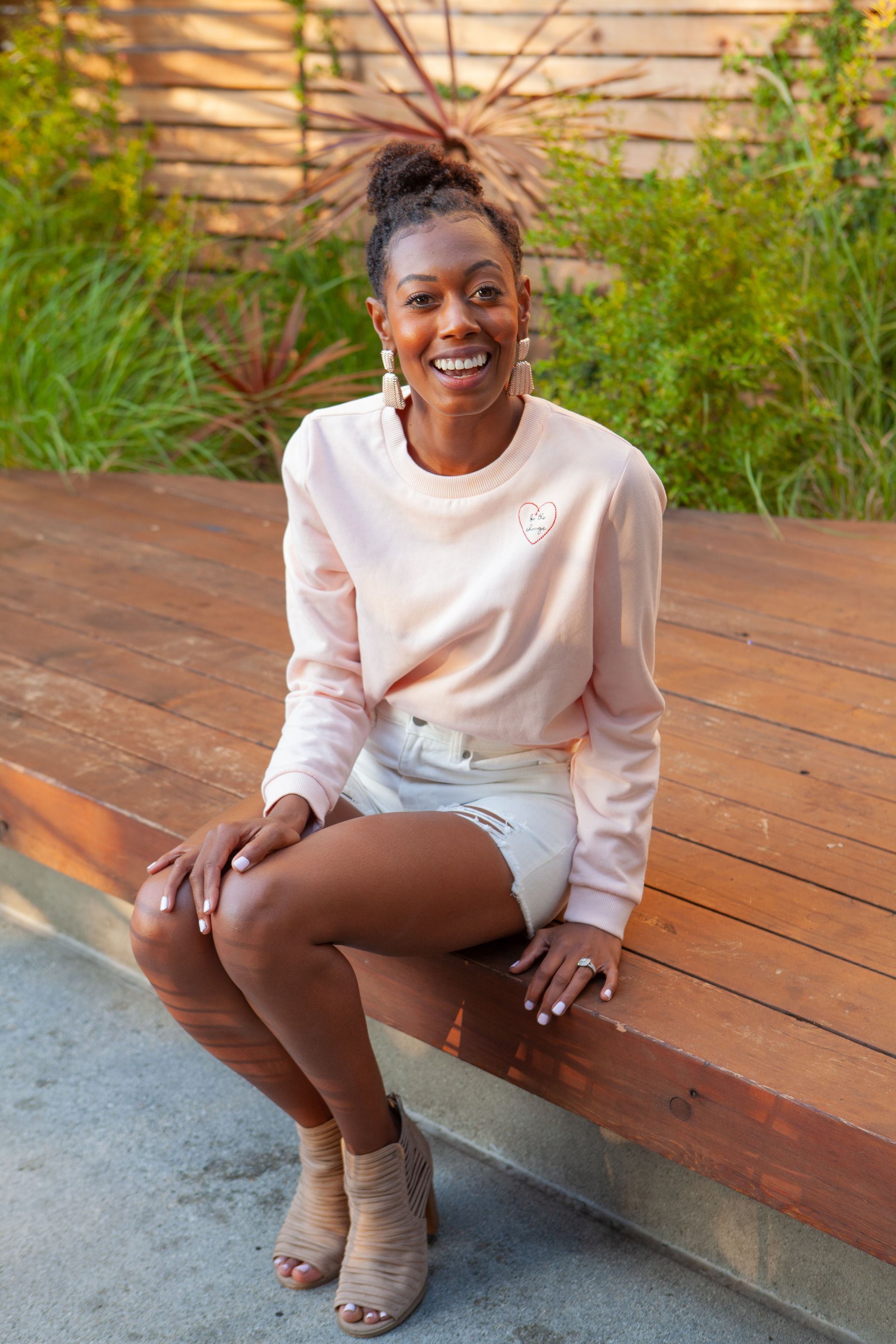 A woman in a white tank top and a green skirt is standing in front of a concrete wall.