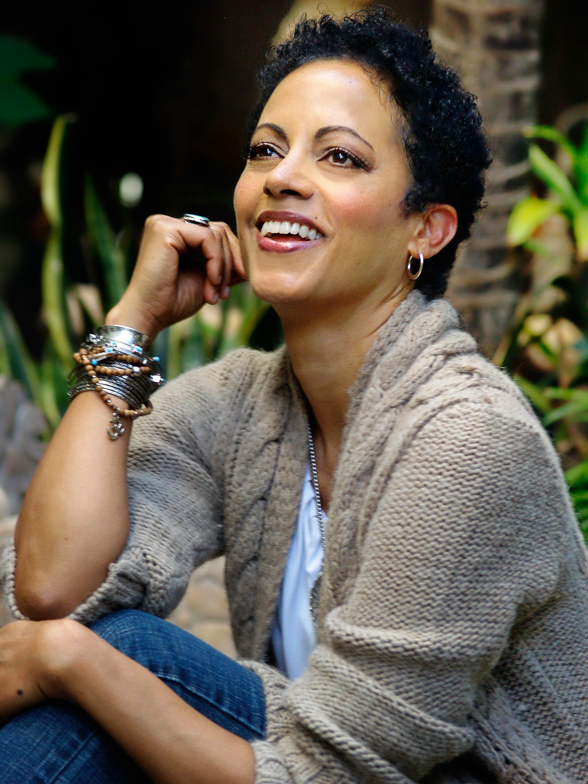 A woman wearing a sweater and bracelets is smiling