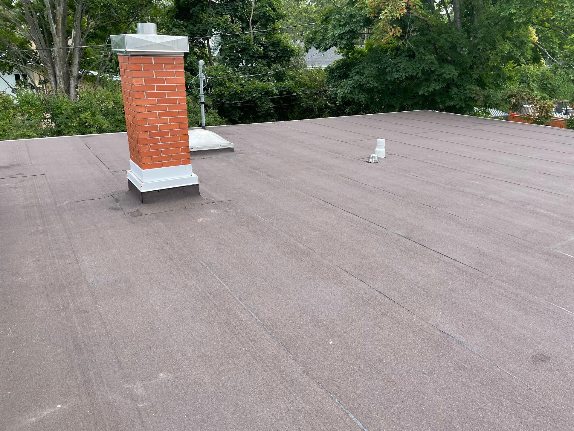 Un toit plat marron avec une cheminée en briques, des arbres en arrière-plan.