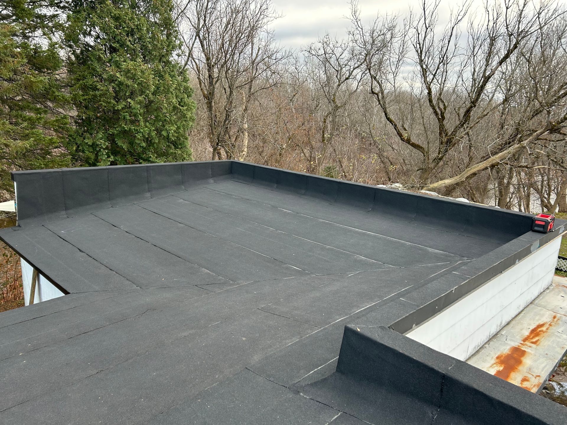 Toit plat et noir sur fond d'arbres et de ciel clair. Une structure aux moulures blanches, avec un peu de rouille visible.