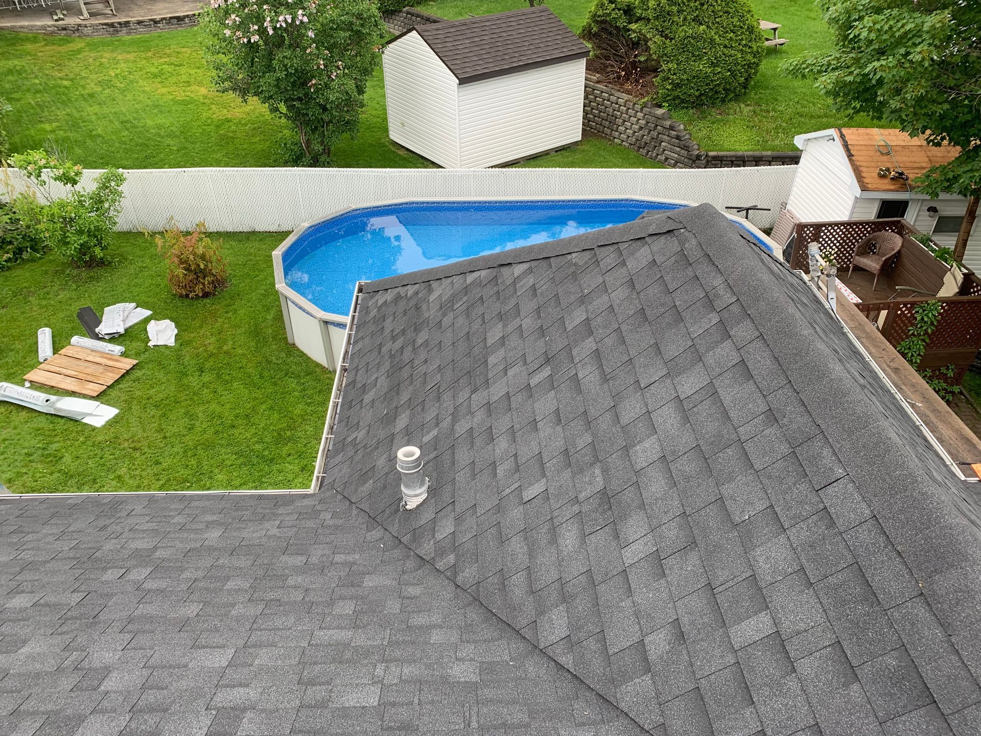 Vue aérienne du toit d'une maison et de l'arrière-cour avec une piscine, une pelouse et un hangar.