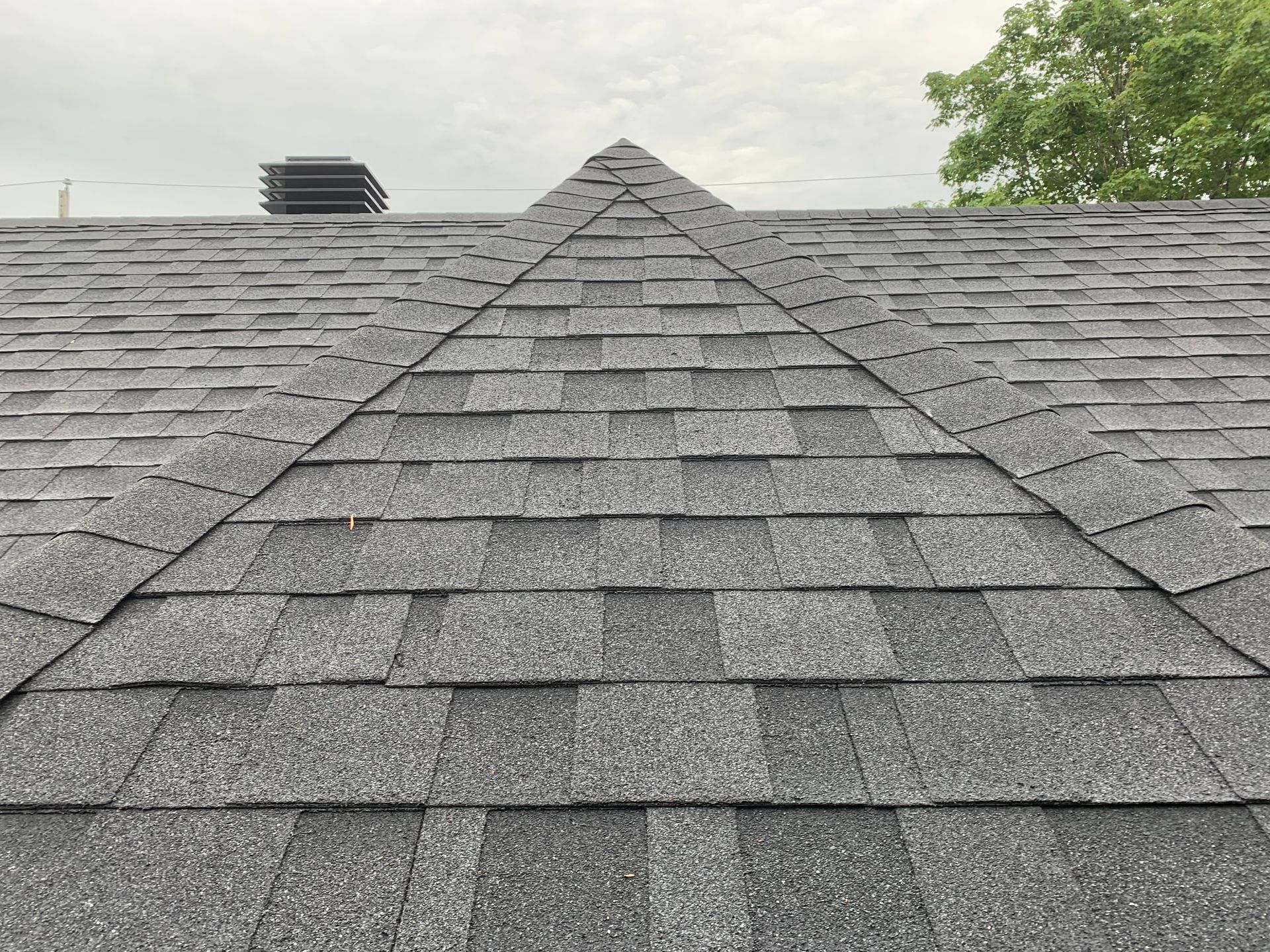 Toit en bardeaux gris avec un sommet triangulaire, un évent et un ciel nuageux en arrière-plan.