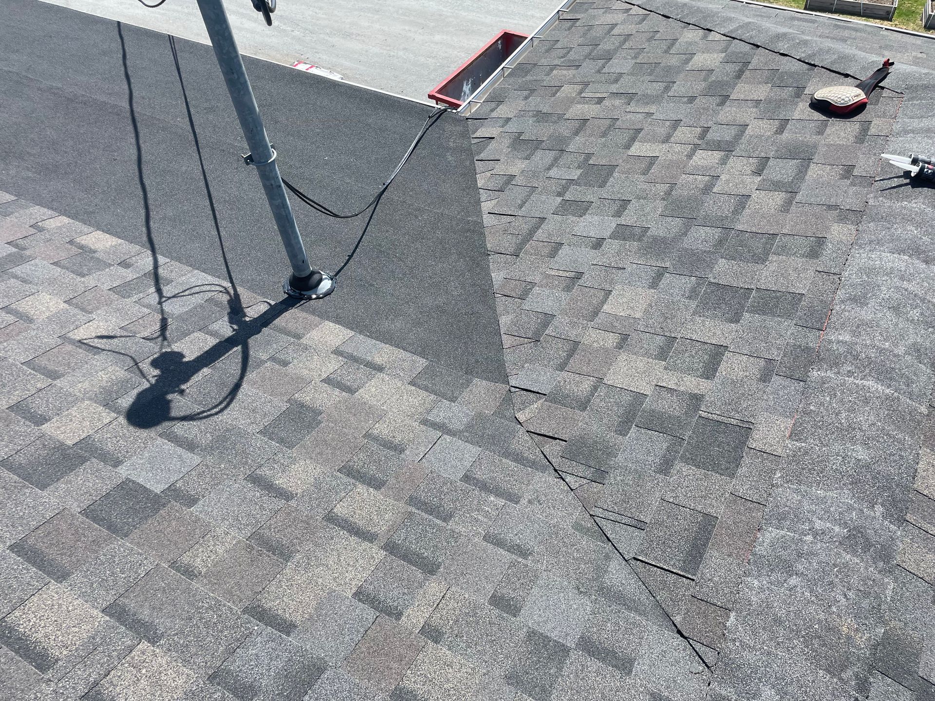 Toiture en bardeaux avec une section de bardeaux neufs gris foncé; poteau avec fils sur le toit.