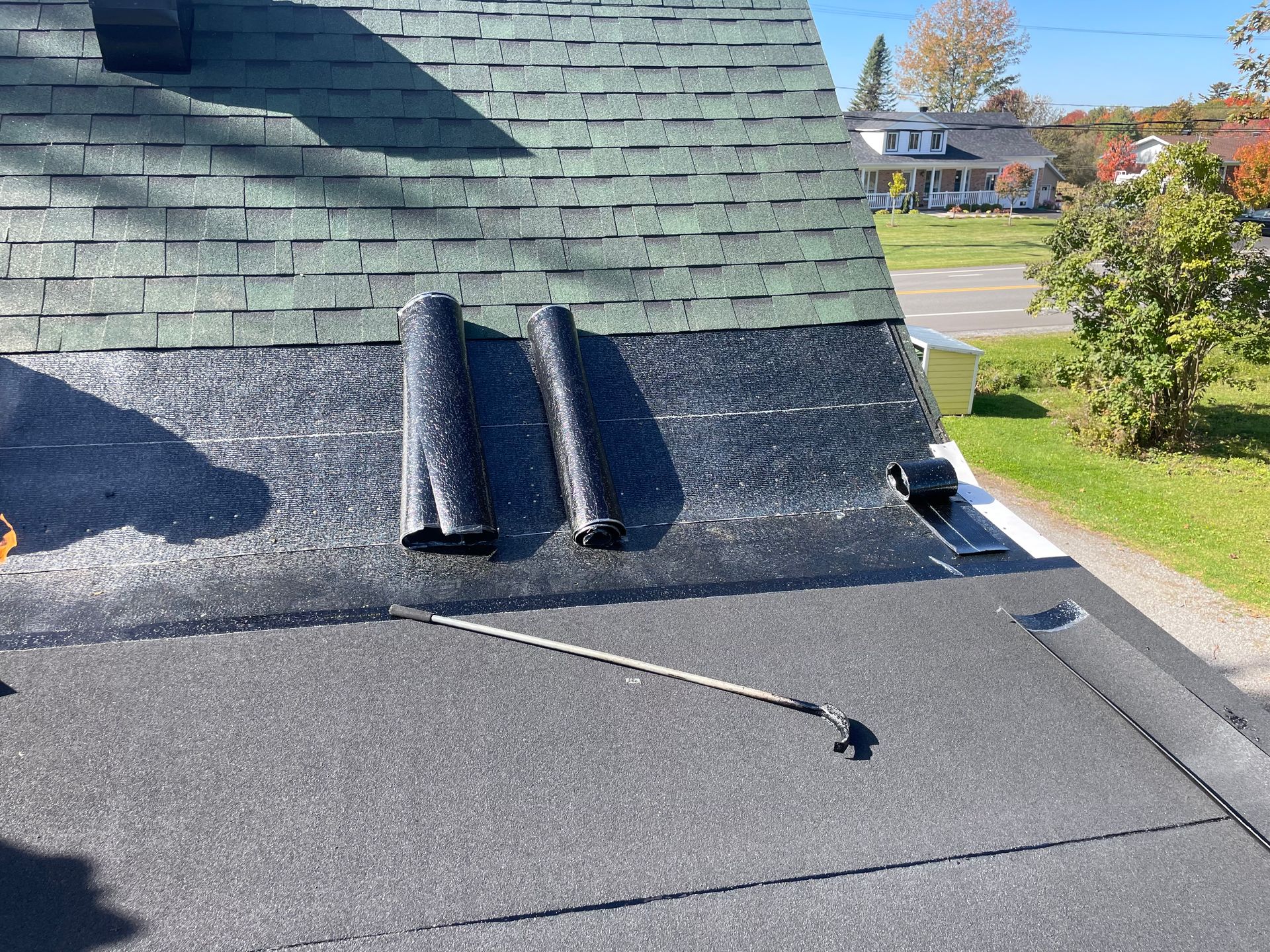 Toiture avec bardeaux verts, toiture roulée noire et outils, à l'extérieur à la lumière du jour.