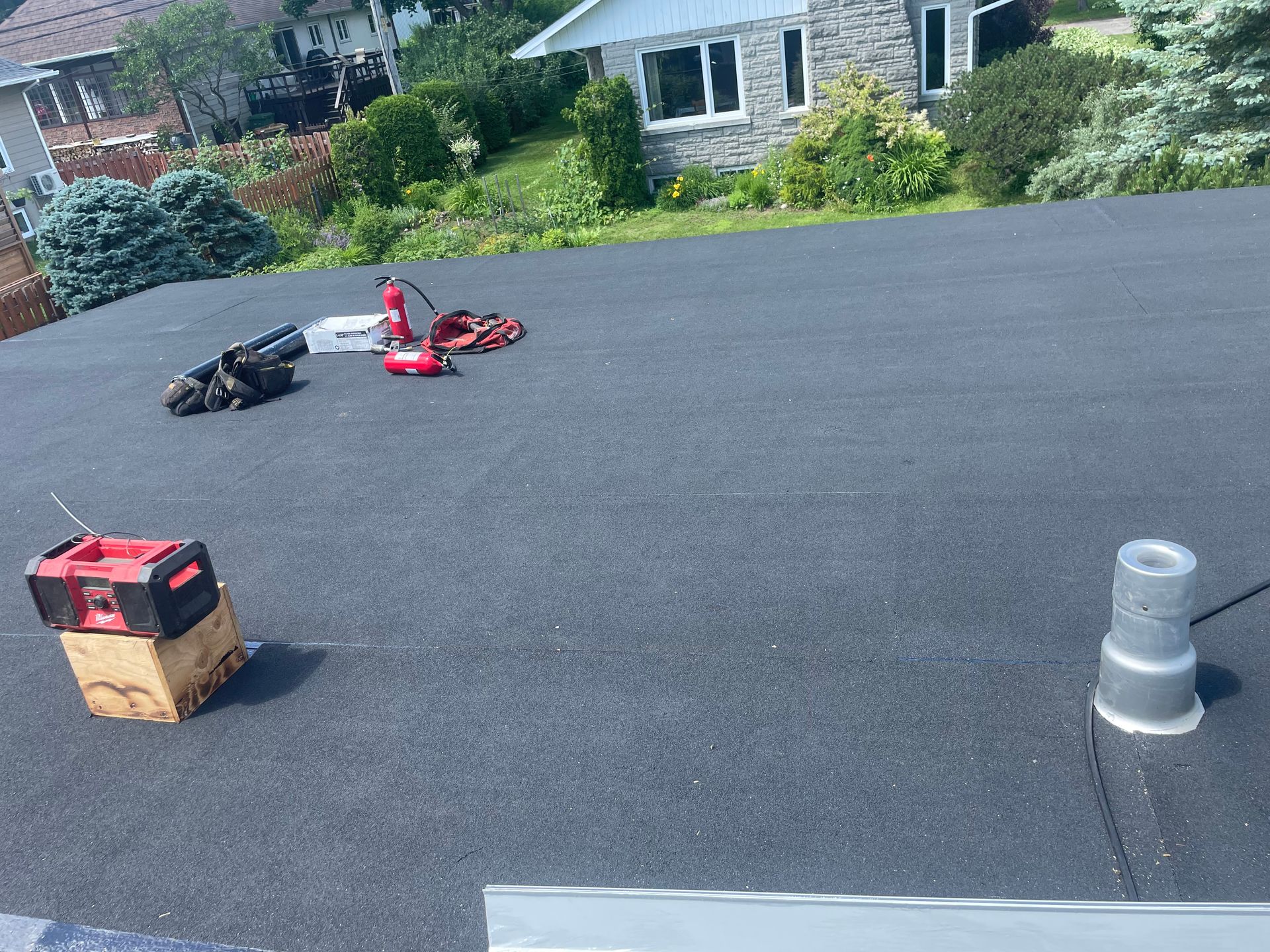 Toit plat noir avec outils ; maison en arrière-plan.