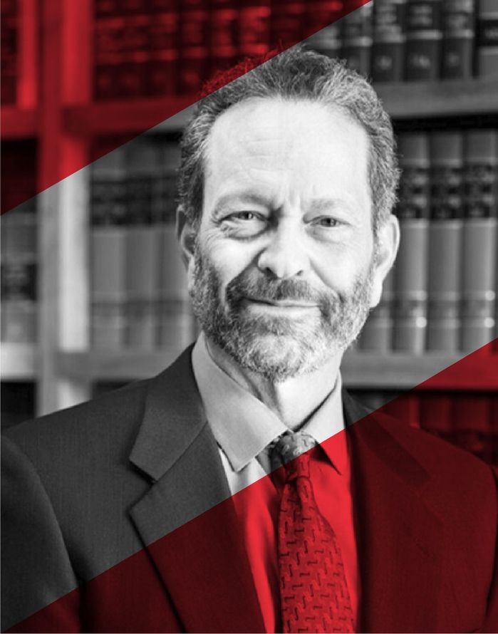 A man in a suit and tie is smiling in front of a bookshelf.