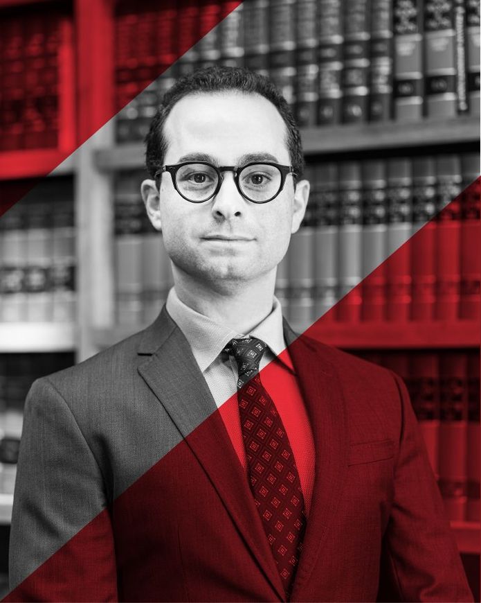 A man in a suit and tie is standing in front of a bookshelf.