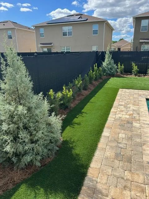 Backyard with black fence, green artificial turf, small trees, and a brick patio.