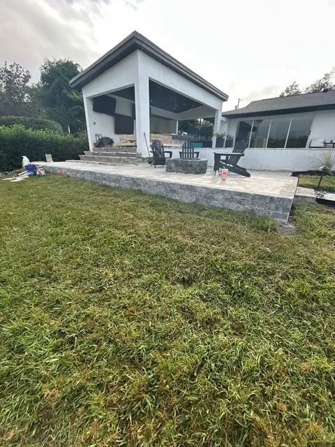A white outdoor structure with a patio, fire pit, and grass lawn.