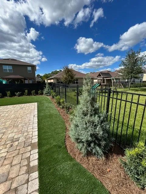 Backyard landscaping with green lawn, black fence, and blue sky.