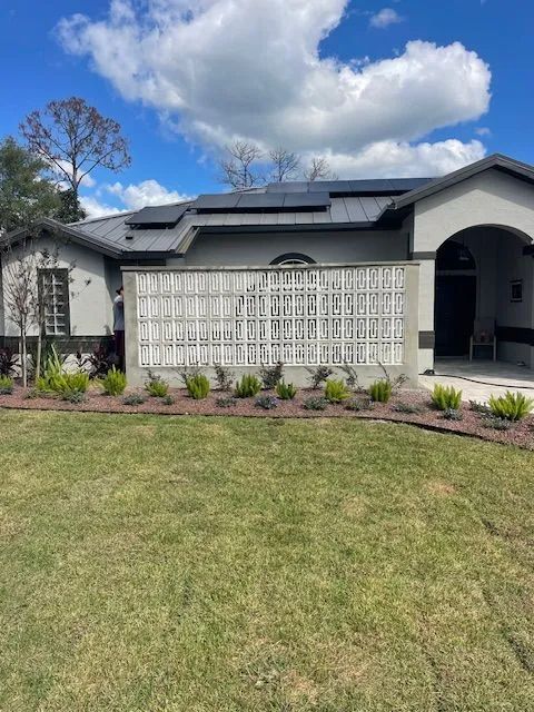 Gray house with a decorative concrete screen, solar panels, and a green lawn under a blue sky.