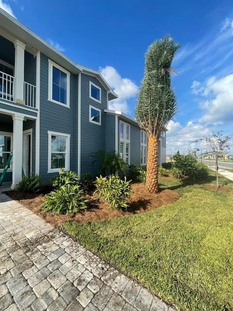 Blue building with landscaping, a palm tree, and a brick walkway under a blue sky.