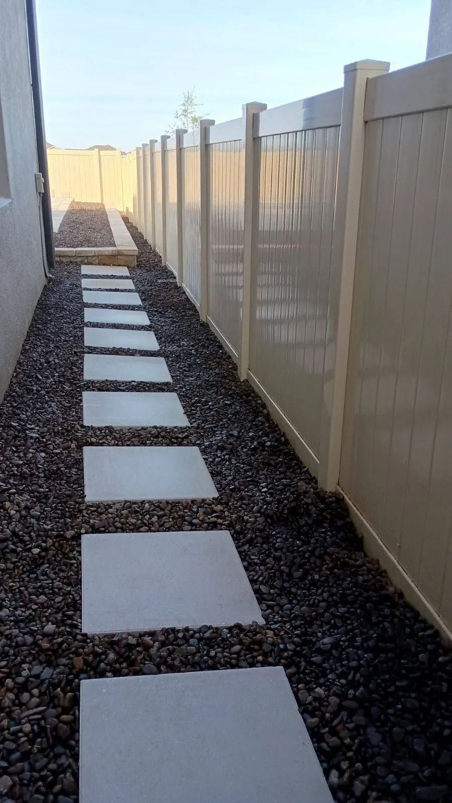Stone path with stepping stones alongside a beige fence and gravel.