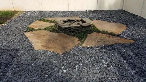 Fire pit with flagstone seating area surrounded by dark gray gravel in a backyard.