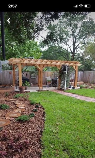 Wooden pergola over a patio in a backyard with a lawn and flowerbeds.