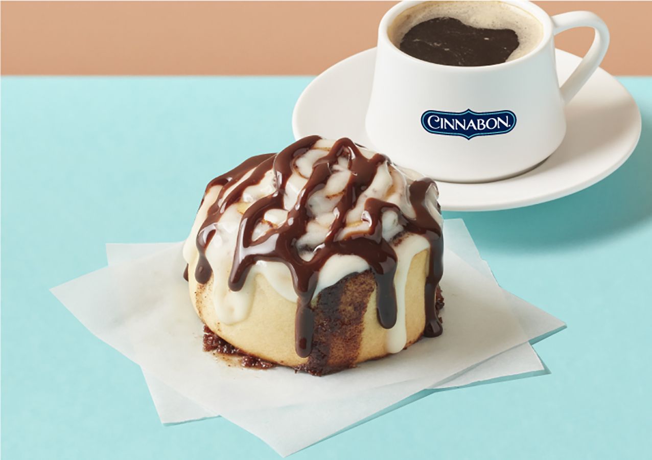 A cinnamon roll is on a napkin next to a cup of coffee.