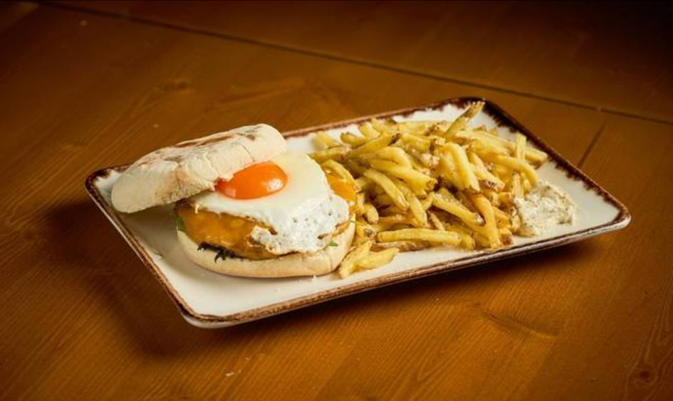 Sanduíche com ovo frito e batatas fritas em um prato retangular branco.