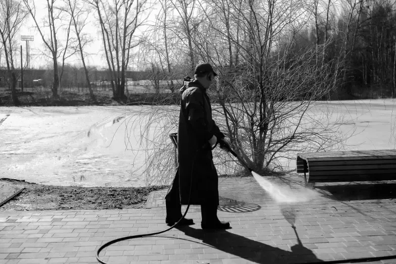 A black and white photo of a man using a high pressure washer on a sidewalk.