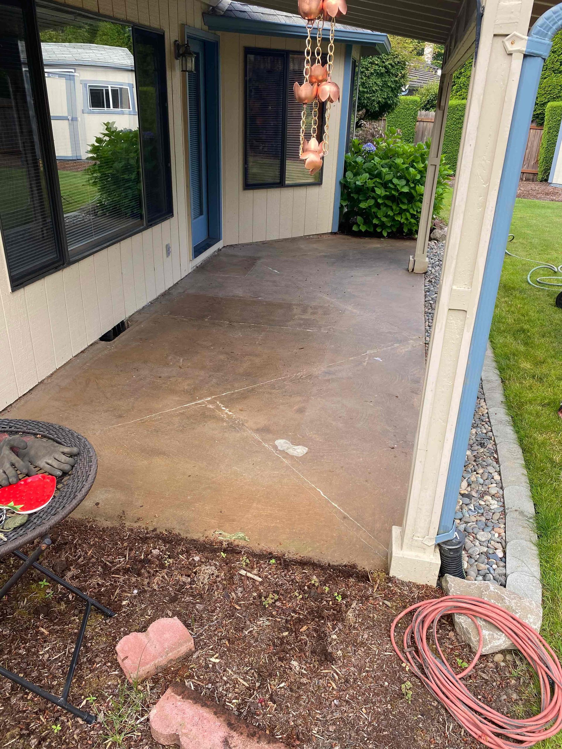 Before Picture of a patio with a table and a hose in front of a house.