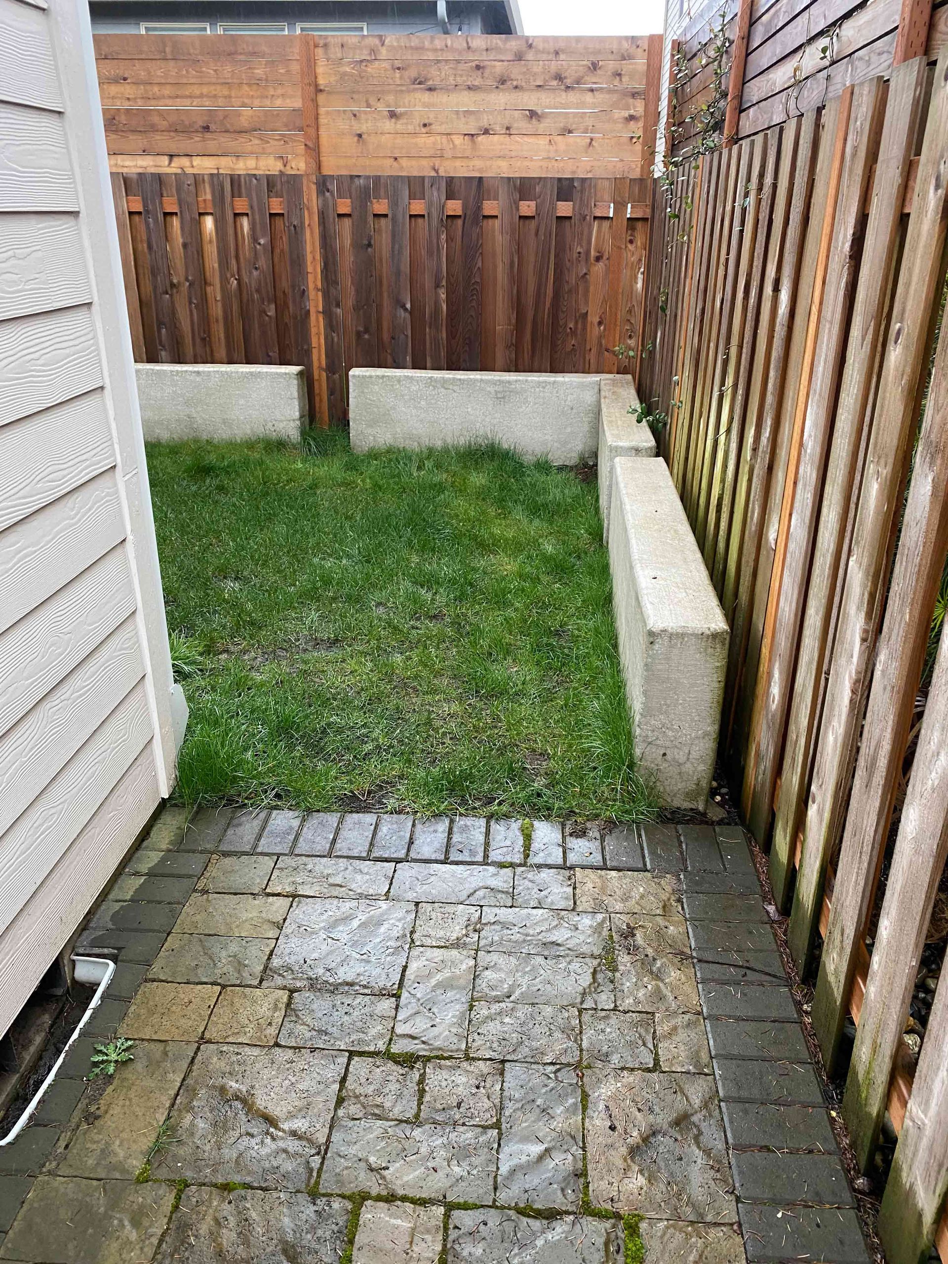 A brick walkway leading to a grassy yard with a wooden fence in Portland OR