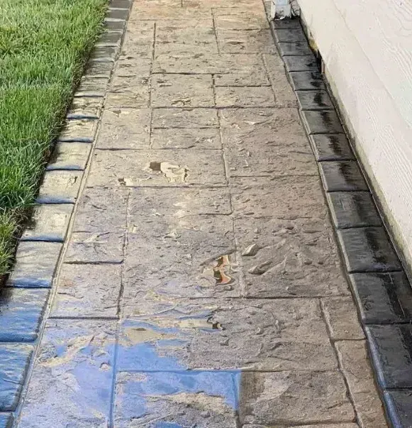A stamped concrete walkway leading to a house next to a lush green lawn.