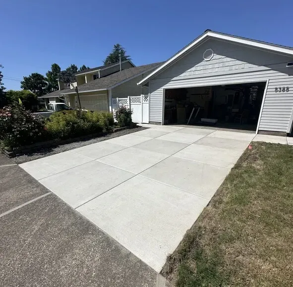 New concrete driveway in front of a light-colored house with an open garage door on a sunny day in Lake Oswego OR.