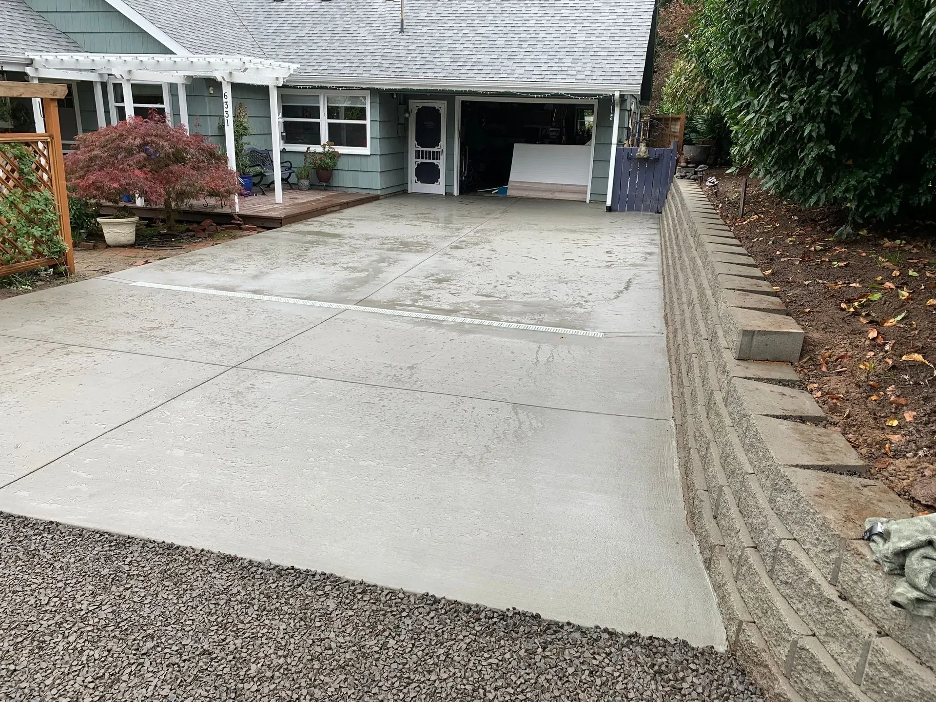 Concrete driveway in front of a house, with a retaining wall on the right and gravel border.