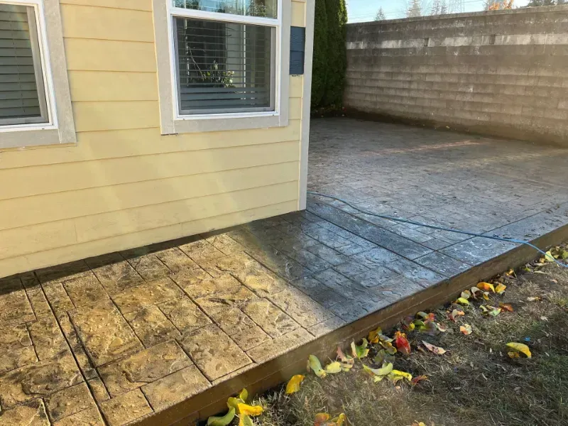 Concrete patio stamped with a textured pattern next to a yellow house with a window.