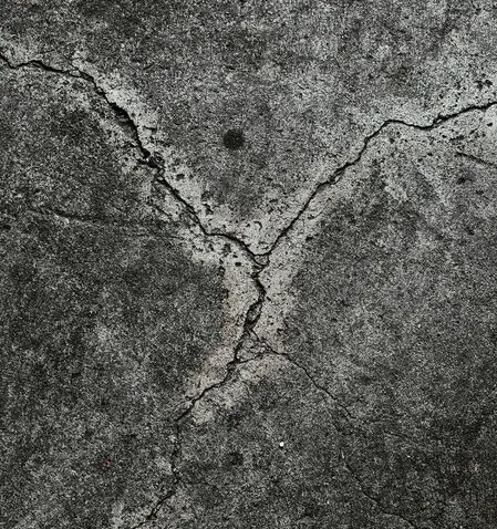 Cracked, grey concrete surface with a prominent Y-shaped fissure and a dark spot.