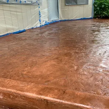 Brown stamped concrete patio, partially wet, with a building in the background covered in protective plastic sheeting.
