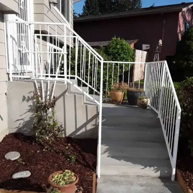 White metal railings frame a concrete set of stairs leading to a building entrance, with potted plants on the landing.