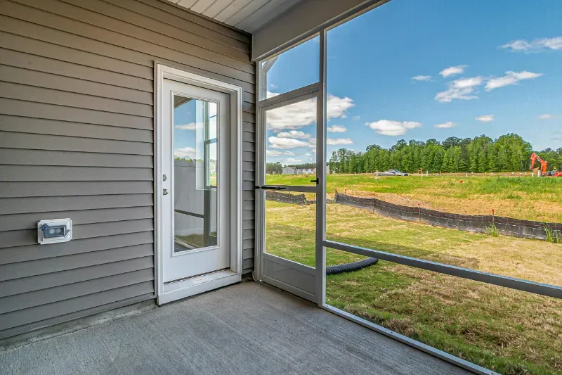 A screened in concrete patio with a door and a view of a field.