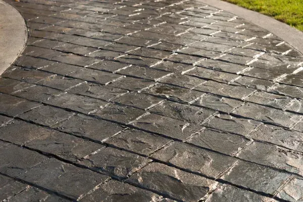 Stamped concrete pathway in a brick pattern, with a curved edge, near grass.