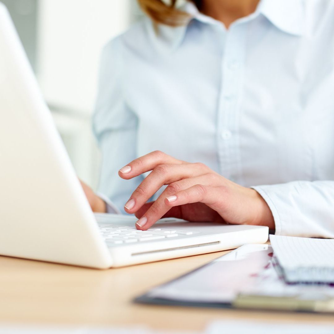 A woman in a white shirt is typing on a laptop