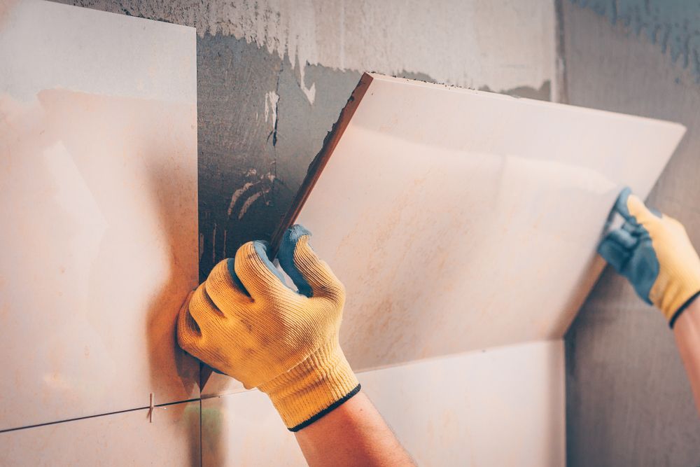 A Person Wearing Yellow Gloves Is Laying Tiles On A Wall — Leakproof in Berkeley, NSW