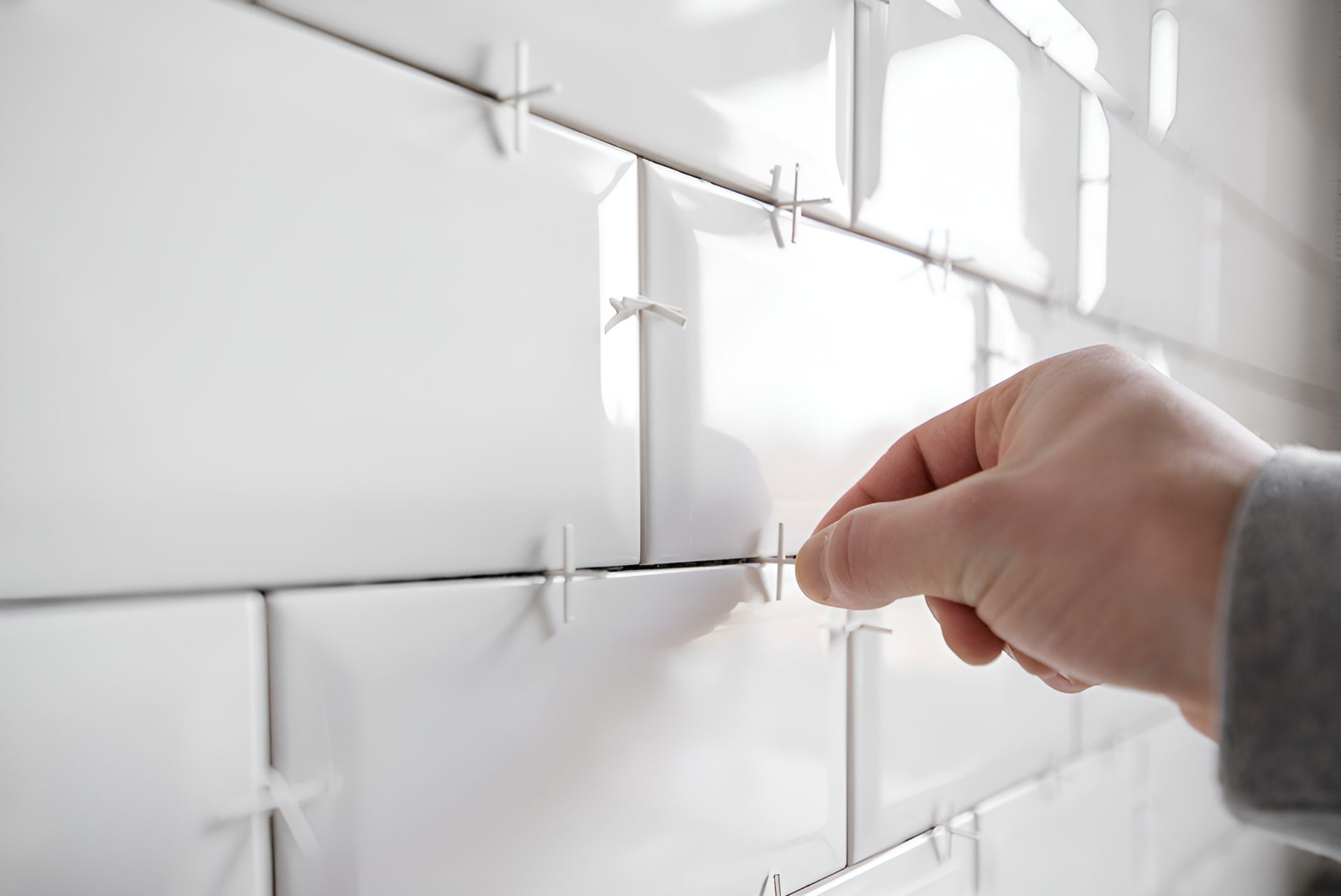 A Person Is Installing White Tiles On A Wall — Leakproof in Berkeley, NSW