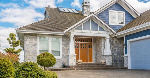 A large house with a blue garage door is sitting on top of a lush green hillside.