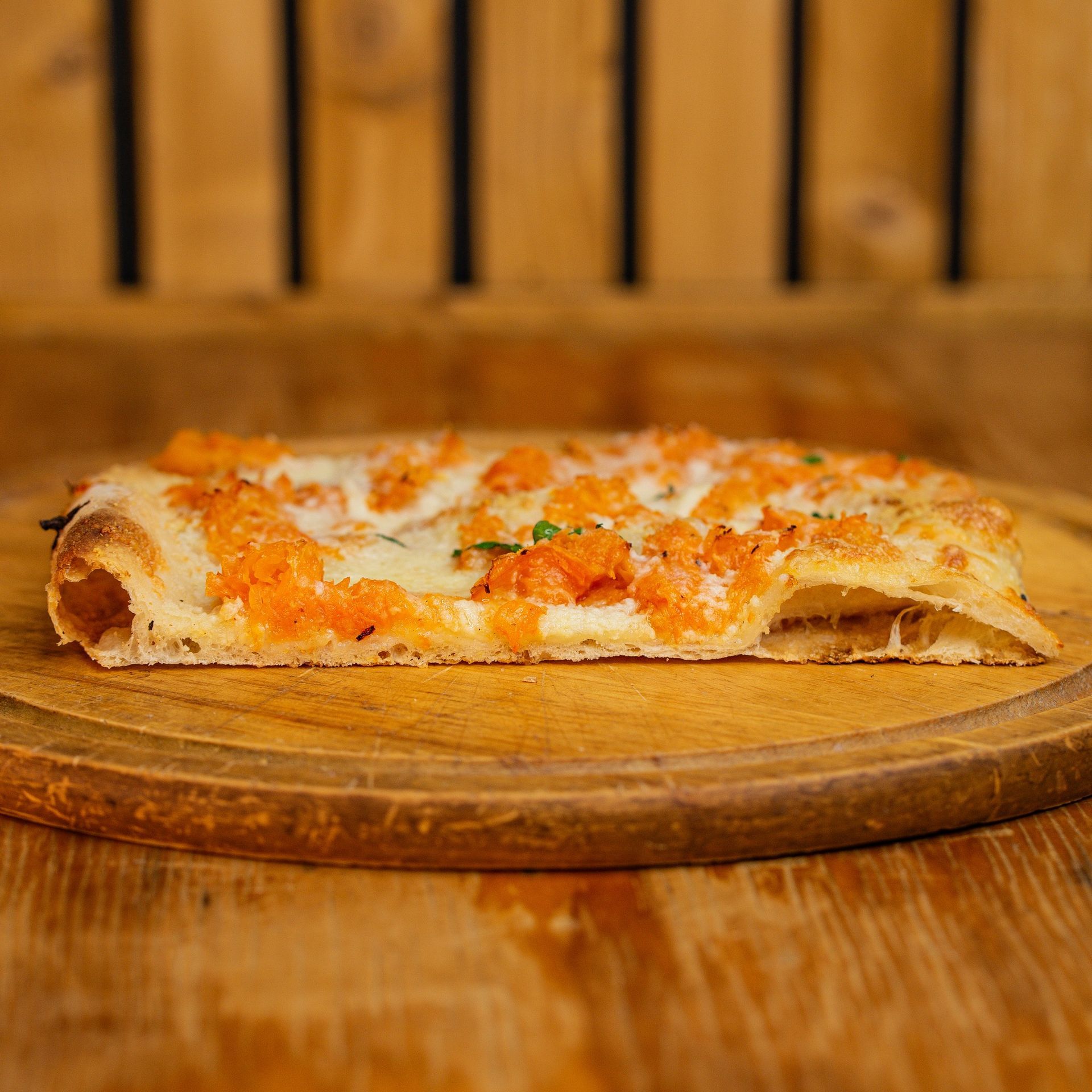 Una fetta di pizza è su un tagliere di legno su un tavolo di legno.
